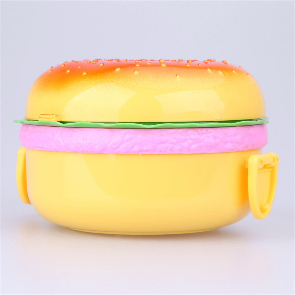 Eine gelbe, burgerförmige Brotdose mit einer grünen Salat- und einer rosa Pattyschicht.