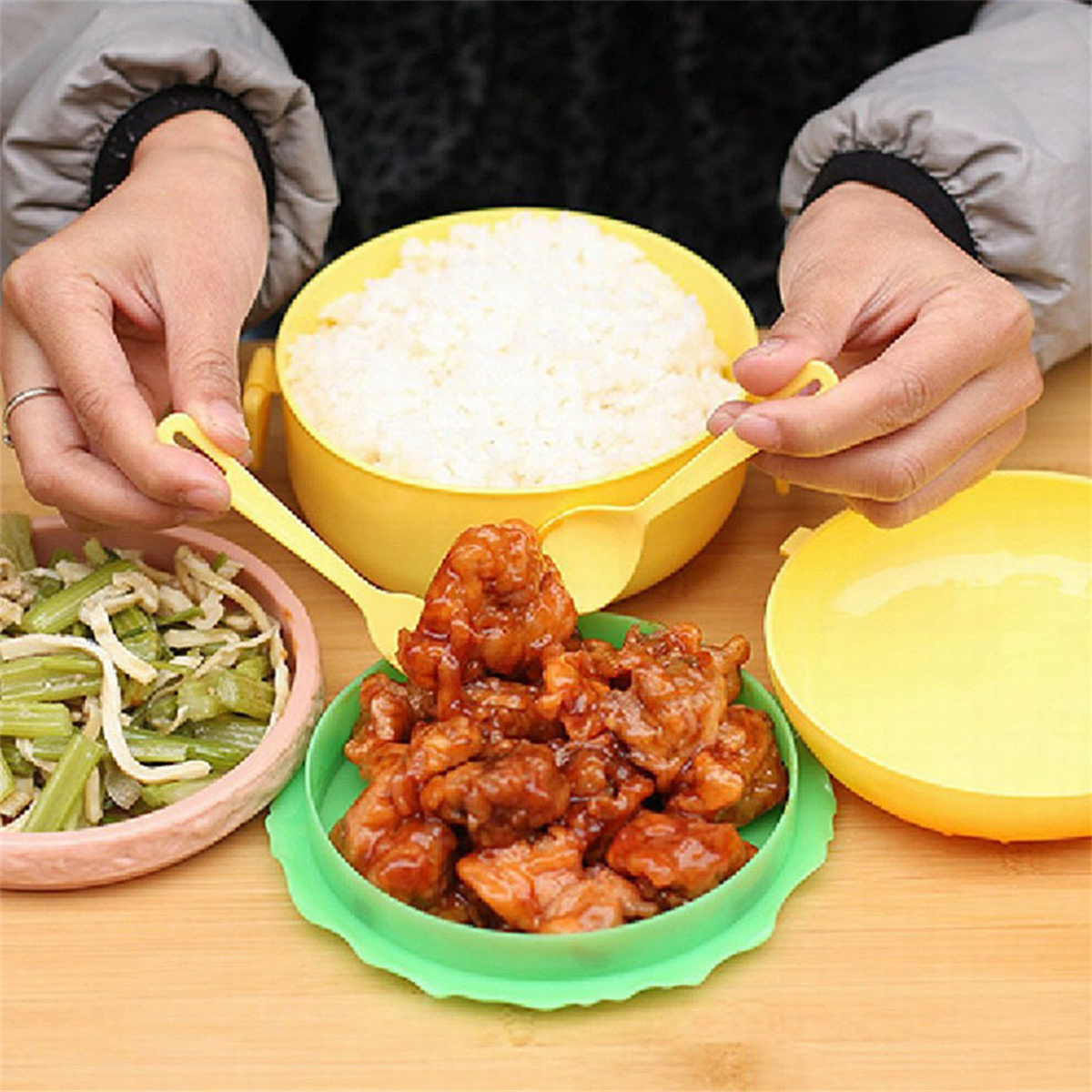 Hände halten eine gelbe Lunchbox mit Reis, Fleisch und Gemüse in Behältern.