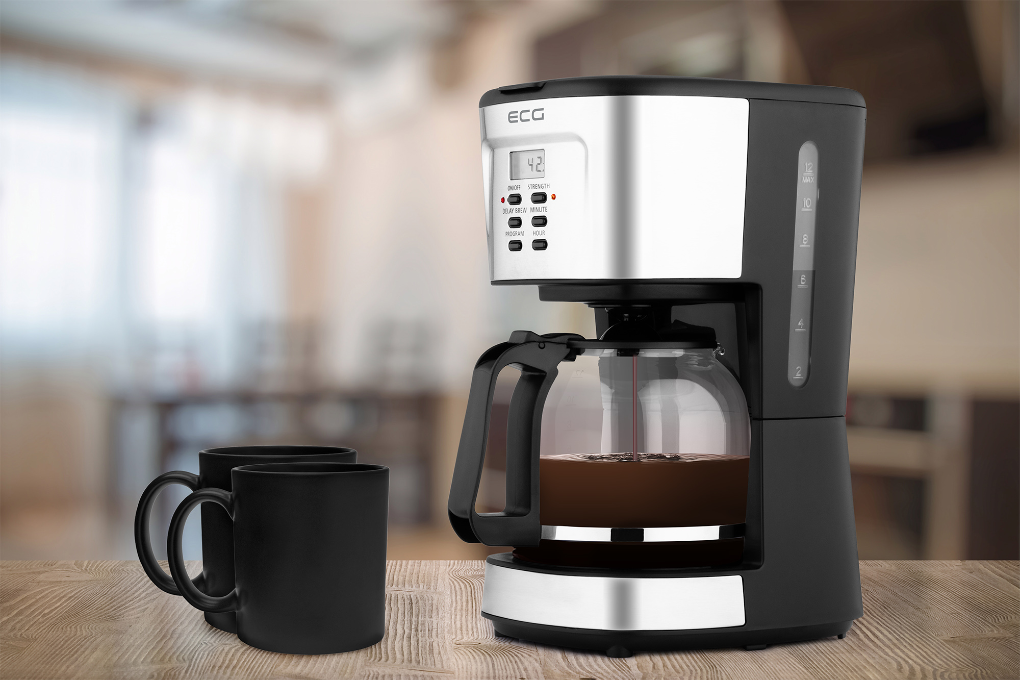 Kaffeemaschine mit Glaskanne, zwei schwarze Tassen auf Holztisch. Küche und verschwommener Hintergrund.