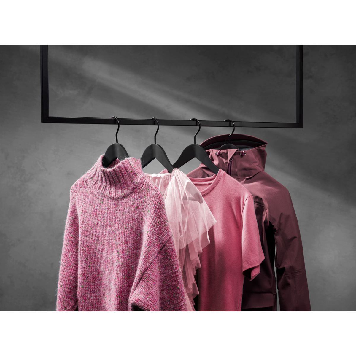 Cztery różowe ubrania wiszące na wieszaku na tle ciemnoszarej ściany. Ubrania obejmują sweter.