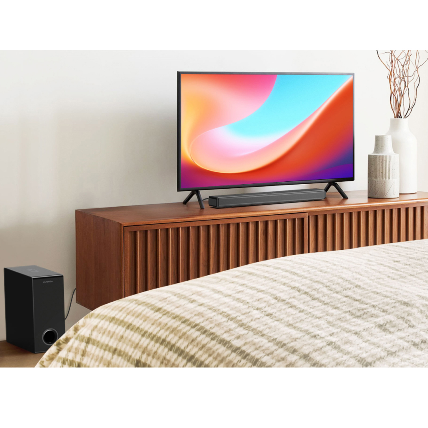 Wohnzimmer mit Fernseher, Soundbar, Subwoofer und Holzschrank. Weiße Wand und Bett.