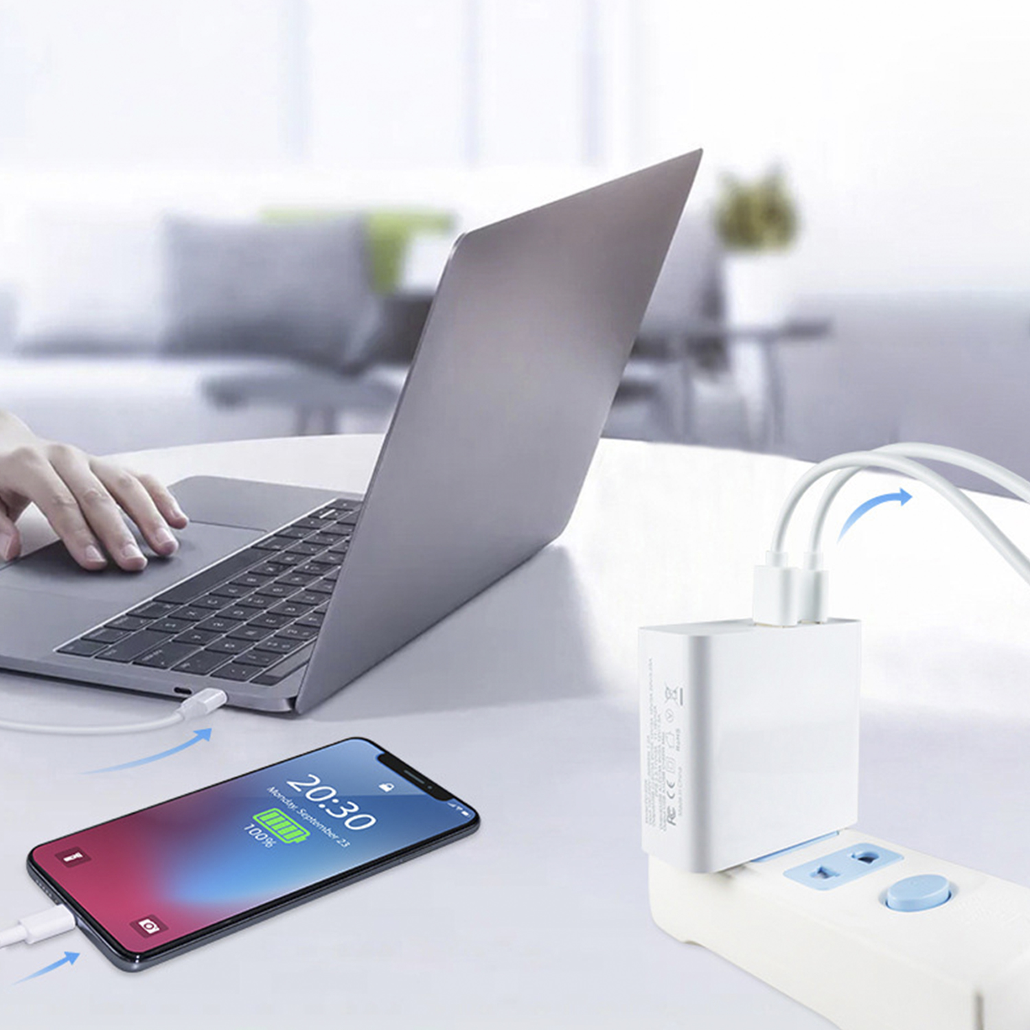 Un laptop, un telefono in carica e un adattatore di alimentazione collegato a una presa su una superficie bianca.