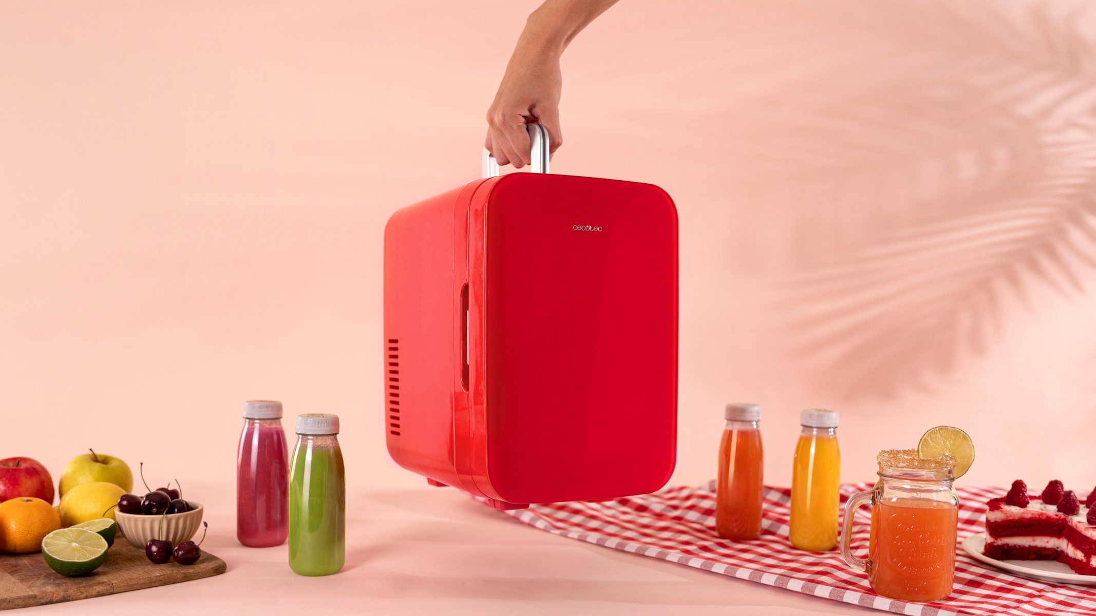 Una mano che tiene un mini frigo rosso. Bottiglie di succo e dessert su una superficie a scacchi.