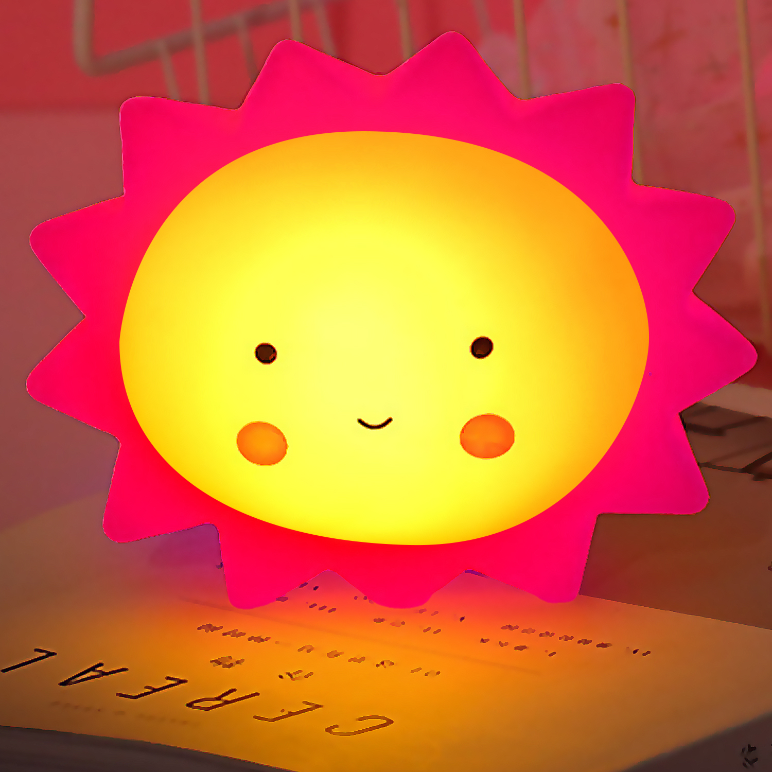 Una luce notturna a forma di sole dei cartoni animati con contorno rosa e faccia gialla su un tavolo.