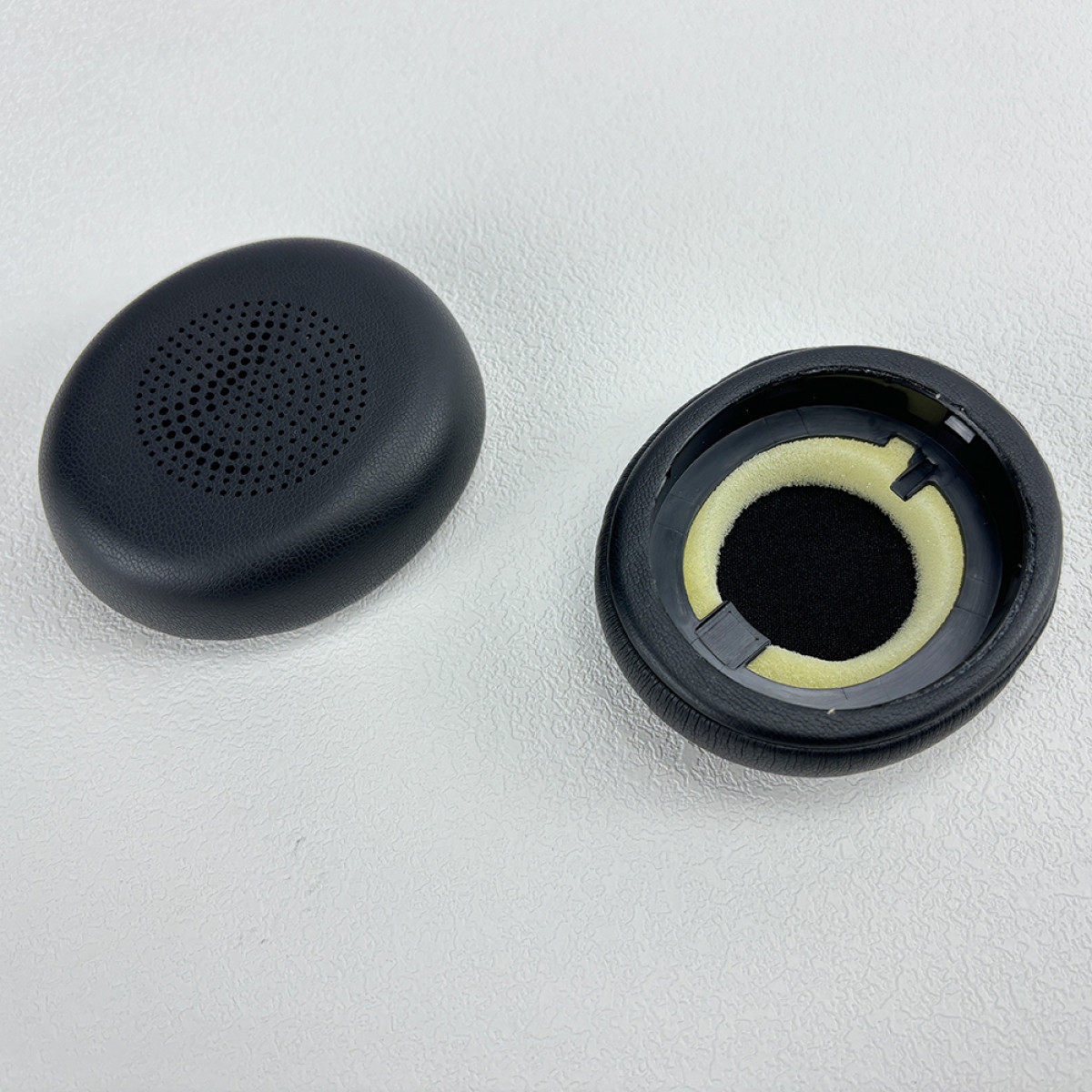 Czarne nauszniki na białej powierzchni. Jeden ma siatkę, drugi otwór.