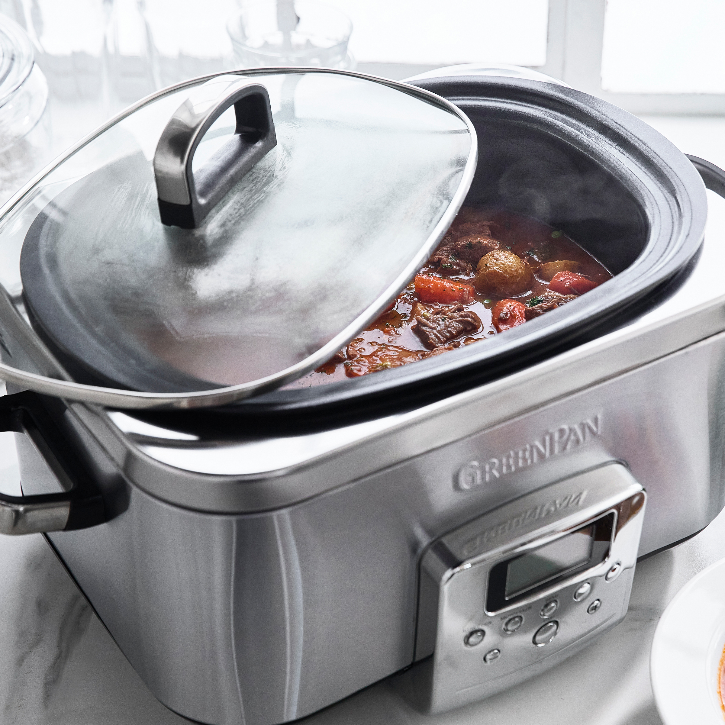 Ein offener Slow Cooker mit Eintopf. Der Deckel liegt daneben. Im Hintergrund ist Licht von einem Fenster zu sehen.