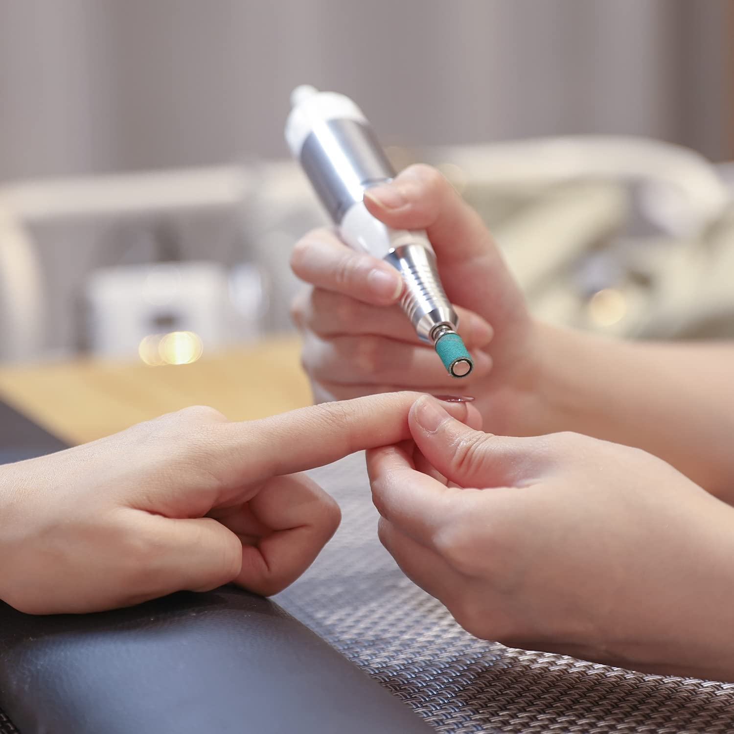 Eine Maniküristin, die einen Nagelbohrer an einem Finger benutzt.