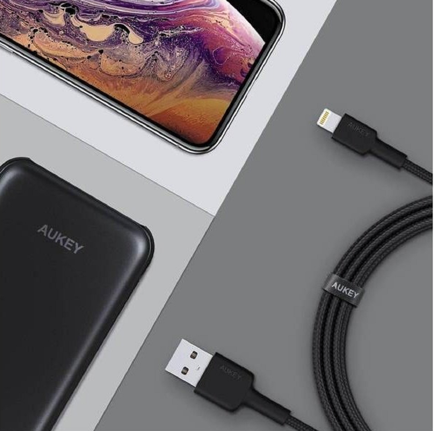Schwarzes Aukey-Ladegerät und Kabelsatz mit einem Telefon. Grauer Hintergrund.