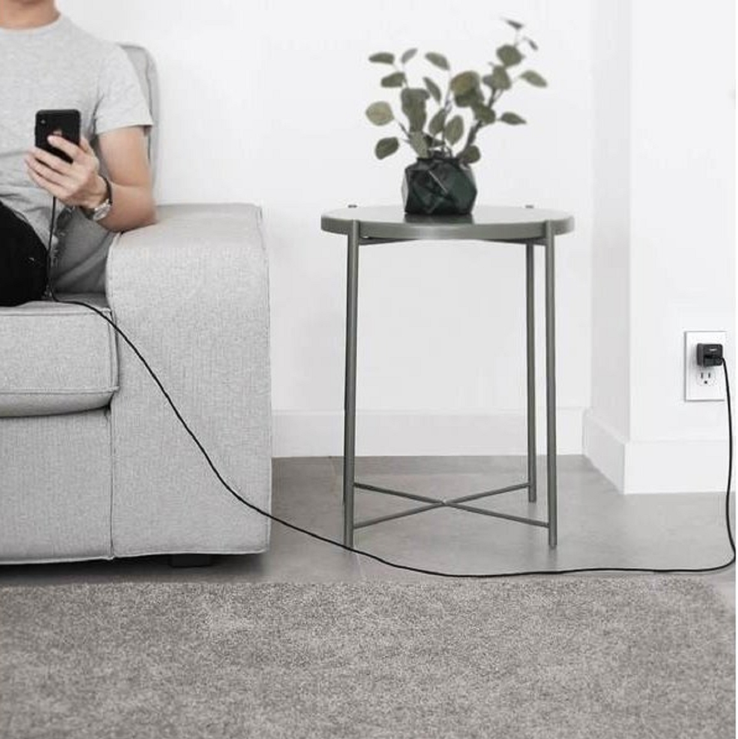 Mann auf Couch benutzt Telefon, lädt es über ein schwarzes Kabel an der Steckdose.
