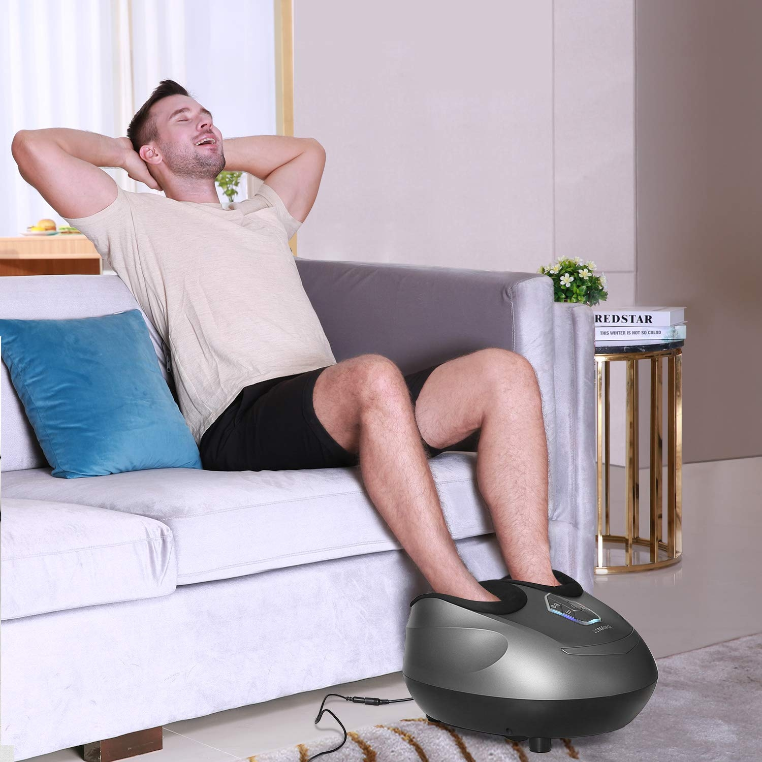 Ein Mann entspannt sich auf einer grauen Couch, mit einem Fußmassagegerät an seinen Füßen.