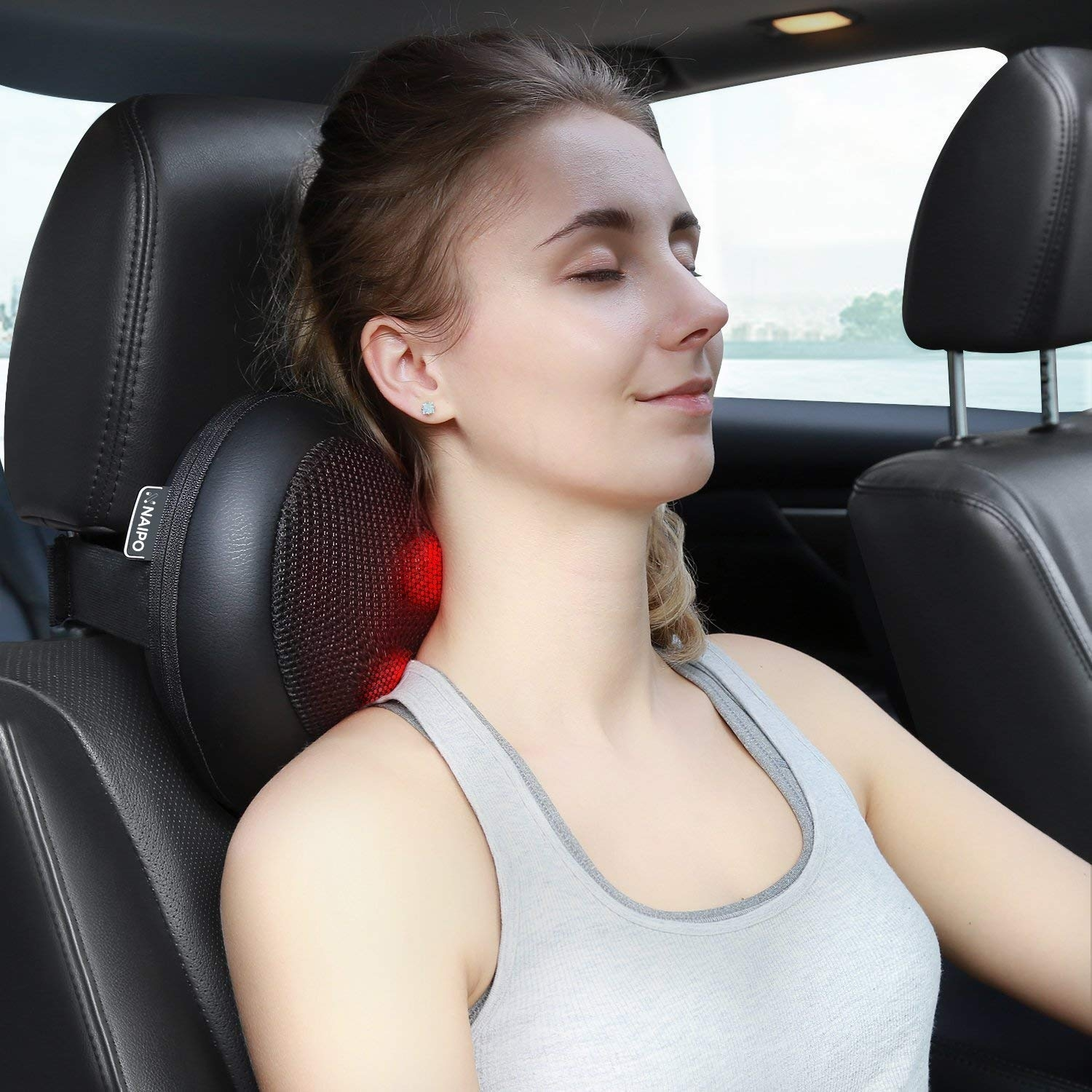 Frau im Auto benutzt ein Nackenmassagegerät. Sie lächelt und hat die Augen geschlossen, genießt die Massage.
