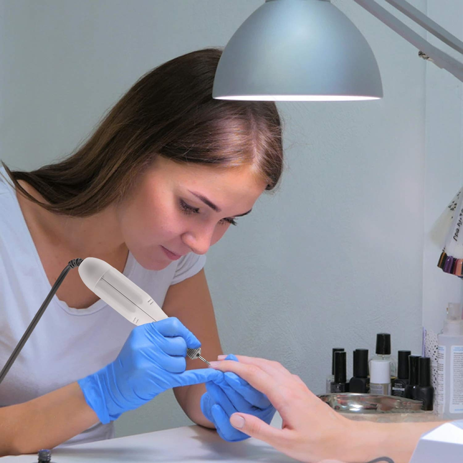 Eine Frau in einem weißen Hemd und blauen Handschuhen macht eine Maniküre. Eine Nagelfräse in ihrer Hand.