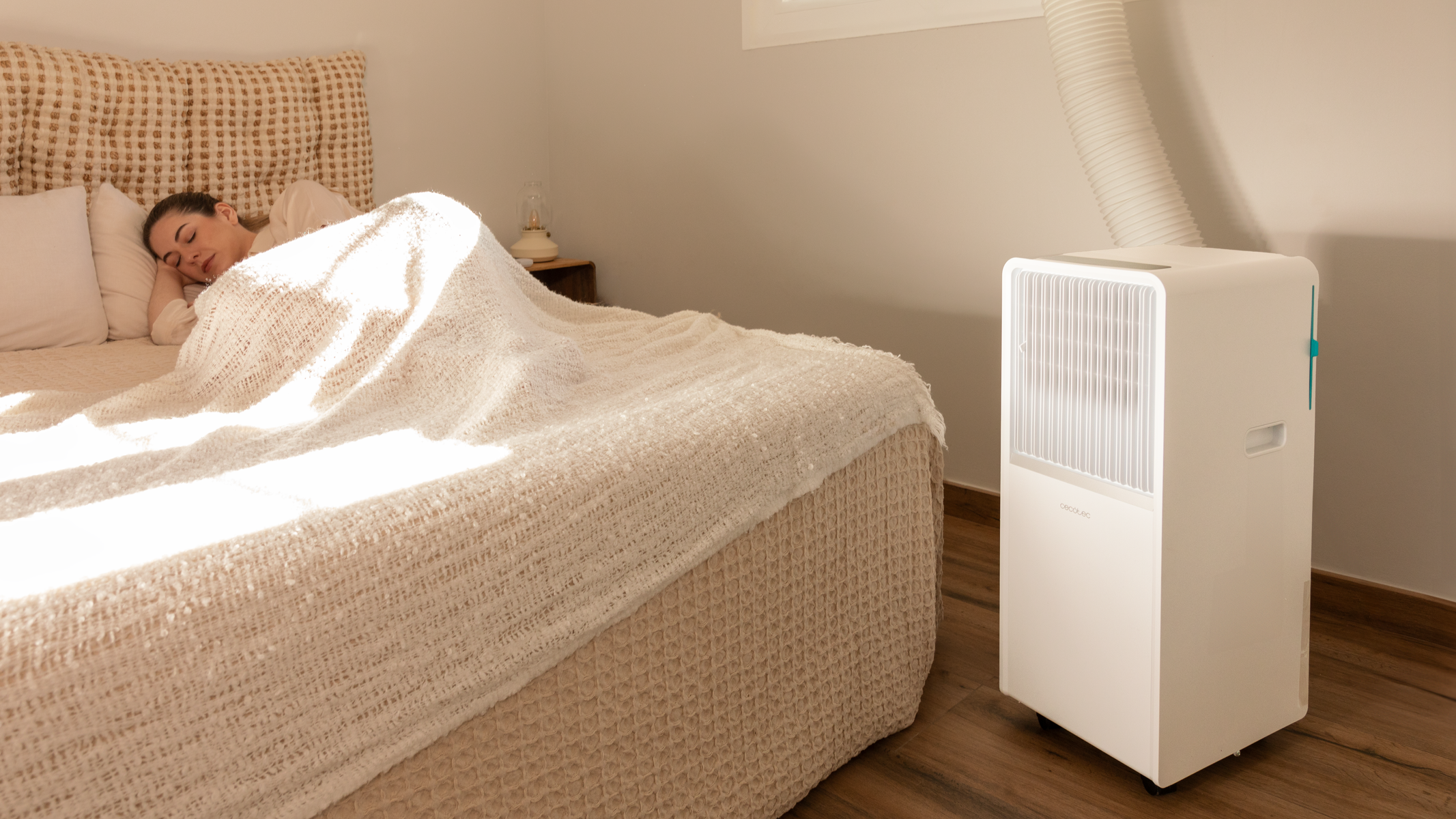 Kobieta śpiąca w łóżku z białym kocem. Przenośny klimatyzator stoi obok łóżka.