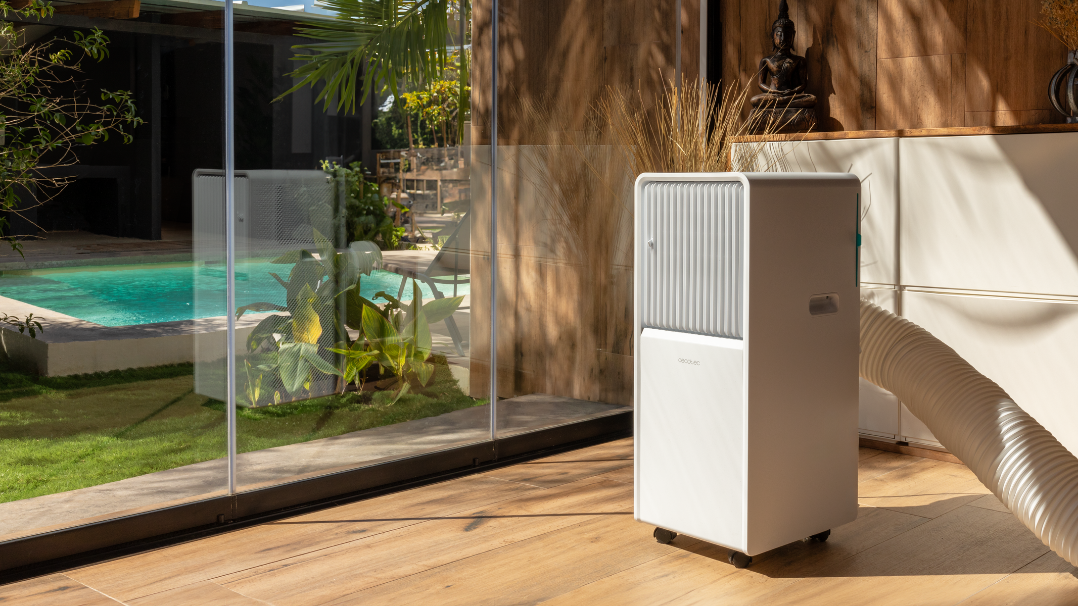Biała jednostka klimatyzacji na drewnianej podłodze obok szklanej ściany z basenem w tle.