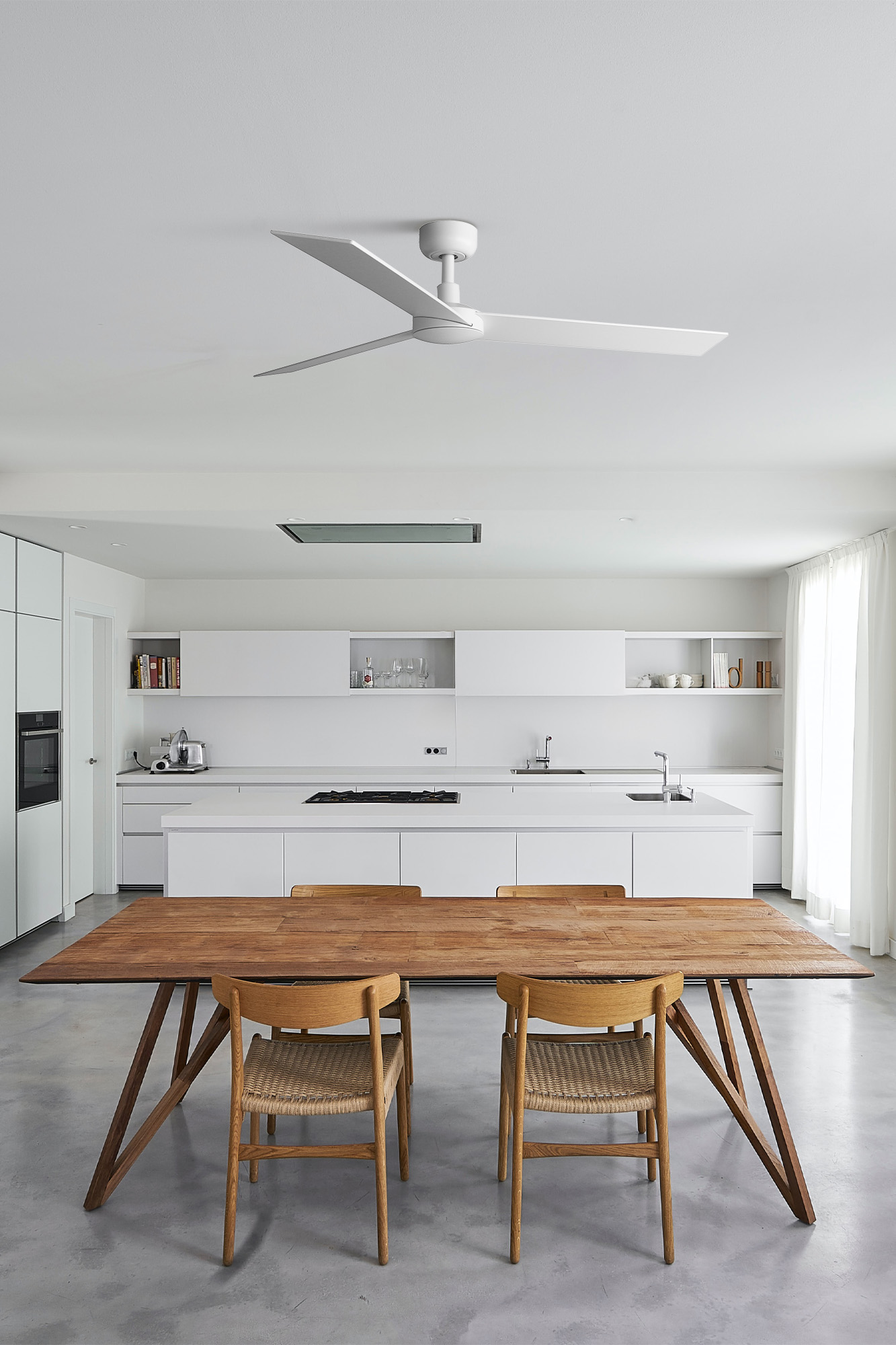 Una moderna cucina bianca con un grande tavolo da pranzo in legno e sedie. Un ventilatore da soffitto è appeso sopra.