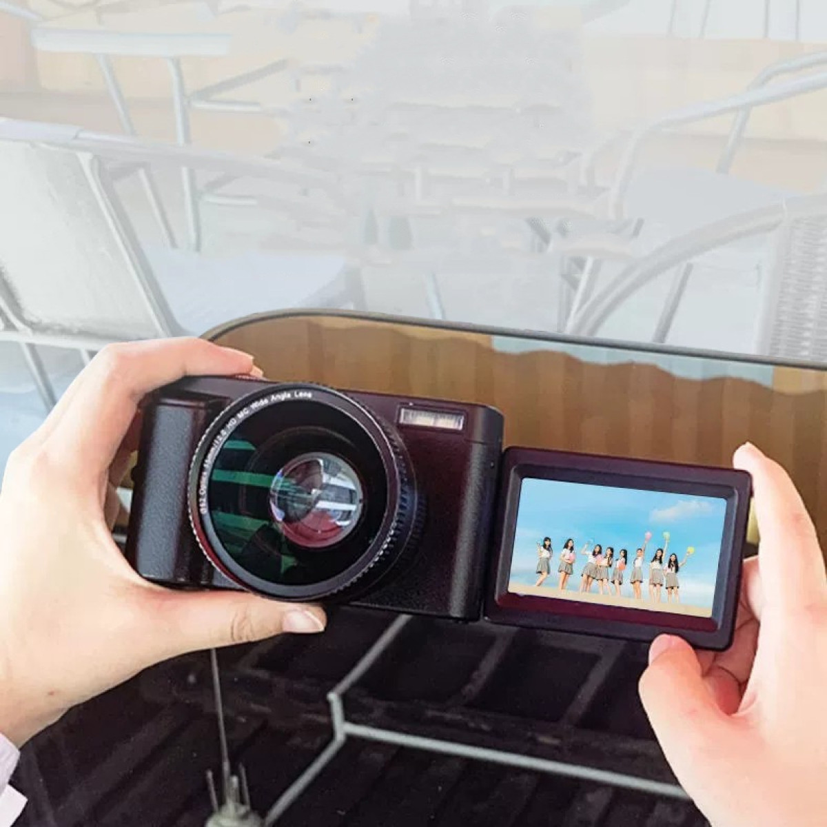 Osoba trzymająca czarny aparat z ekranem pokazującym grupę ludzi, widoczne dłonie.