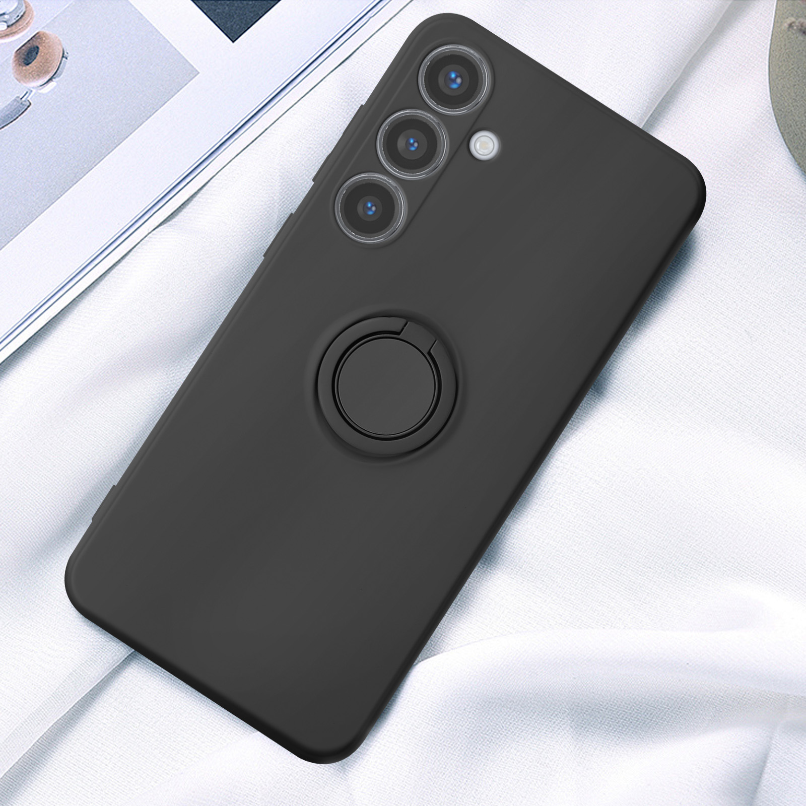 Un telefono nero con un porta anello è appoggiato su un panno bianco. Sono visibili tre obiettivi della fotocamera.