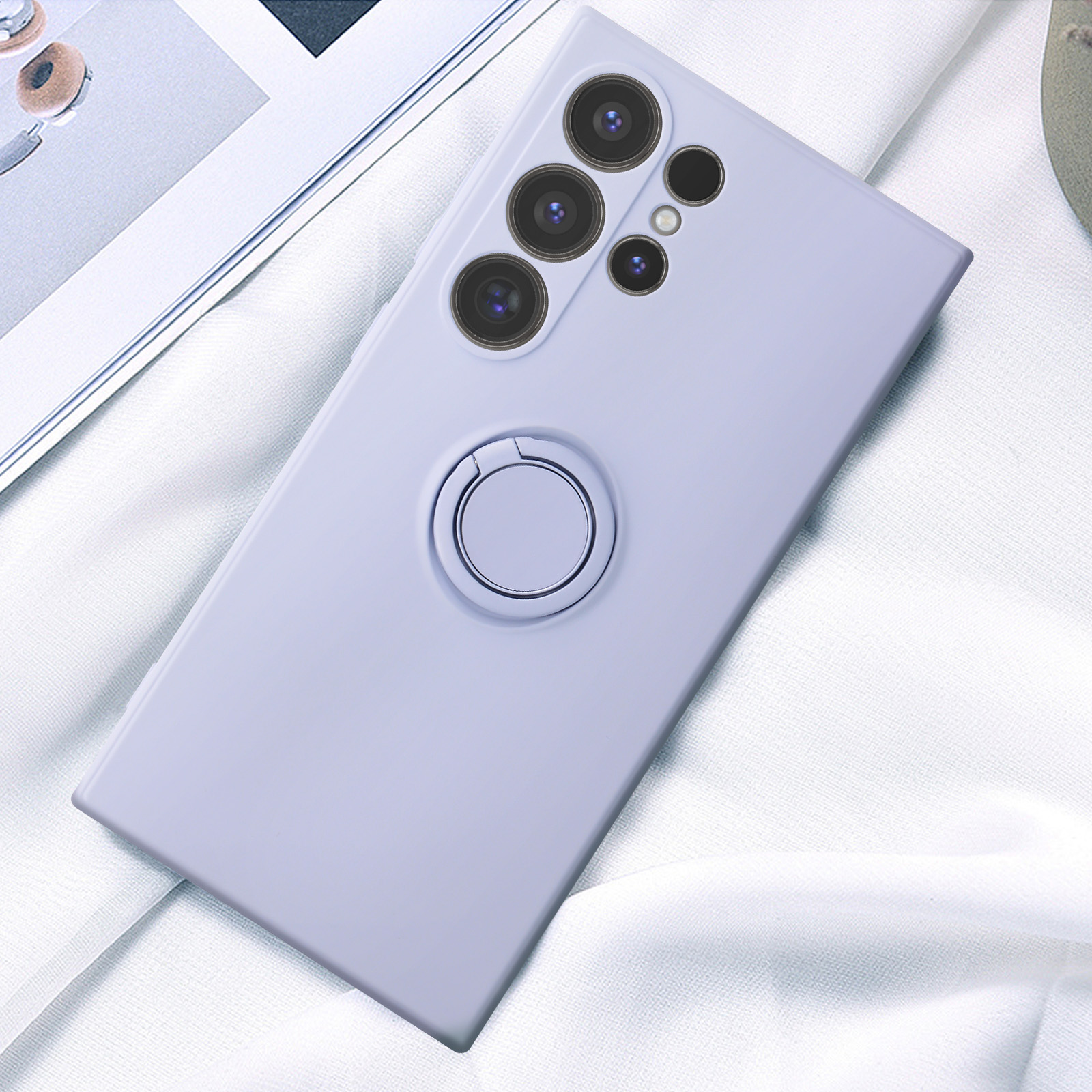 Una custodia per telefono viola chiaro con lenti della fotocamera e un supporto ad anello, su un panno bianco.