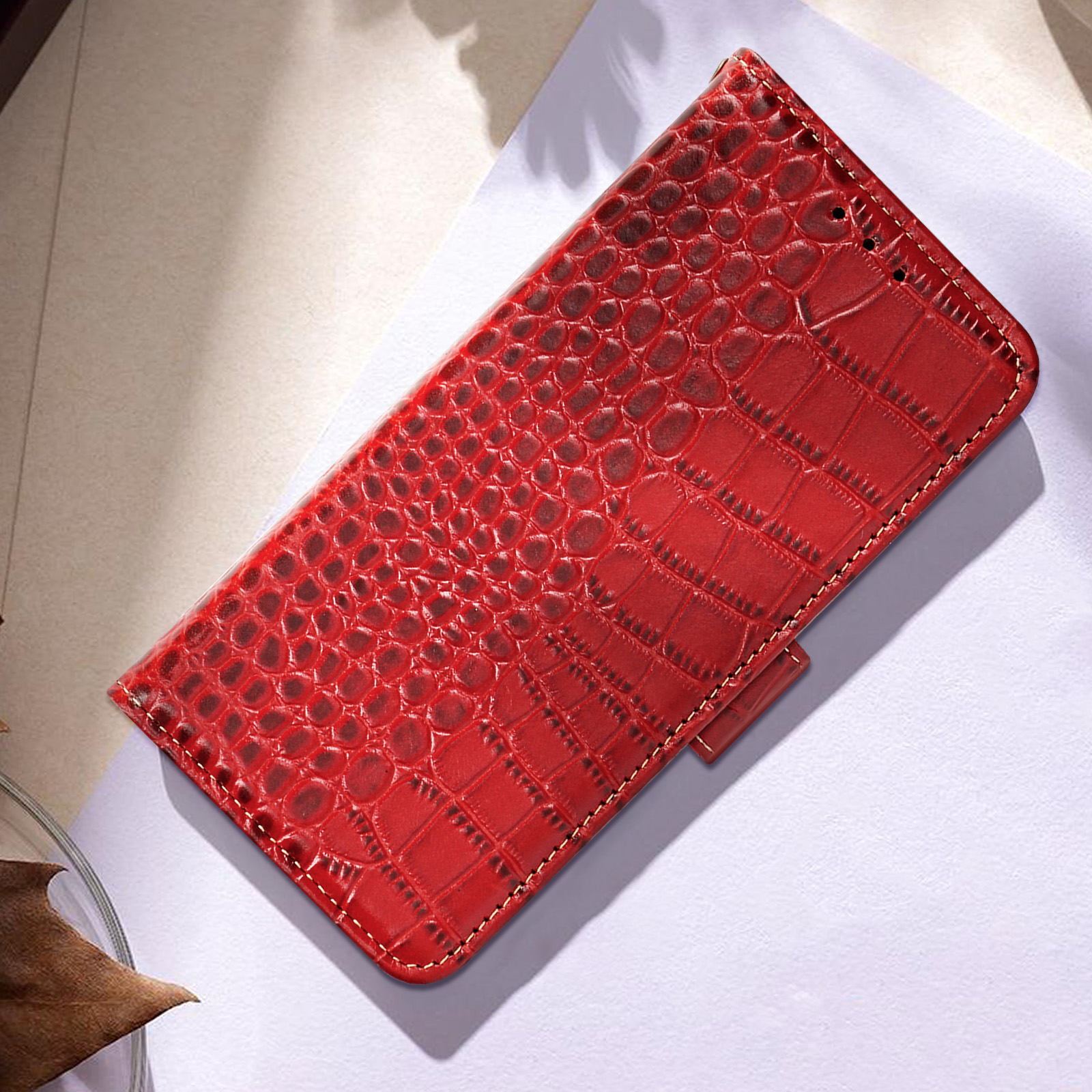 Custodia per telefono in pelle rossa con texture a pelle di coccodrillo, aperta su una superficie chiara, che mostra la fodera interna.
