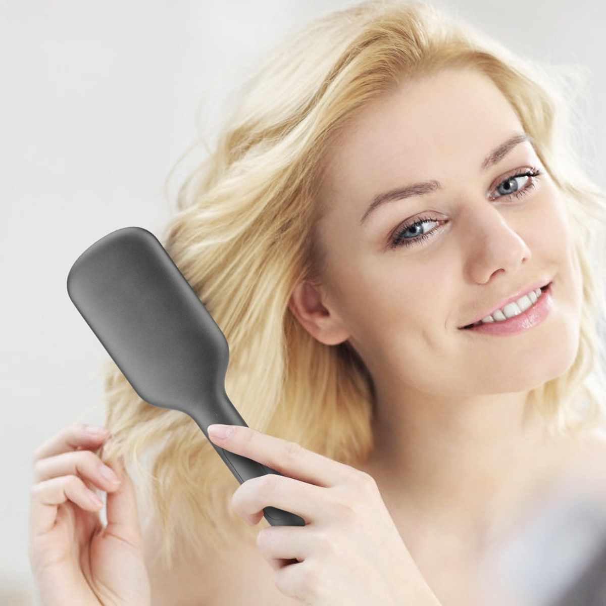 Frau bürstet ihr blondes Haar mit einer grauen, flachen Bürste, lächelnd.