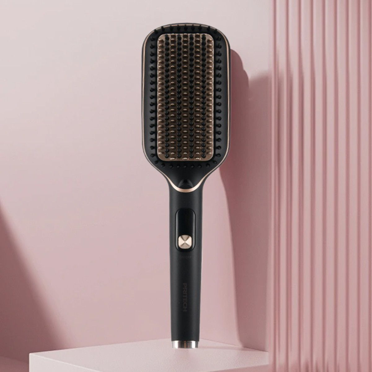 Eine schwarz-goldene Haarglättungsbürste. Sie steht auf einer rosa Oberfläche und hat einen Griff.
