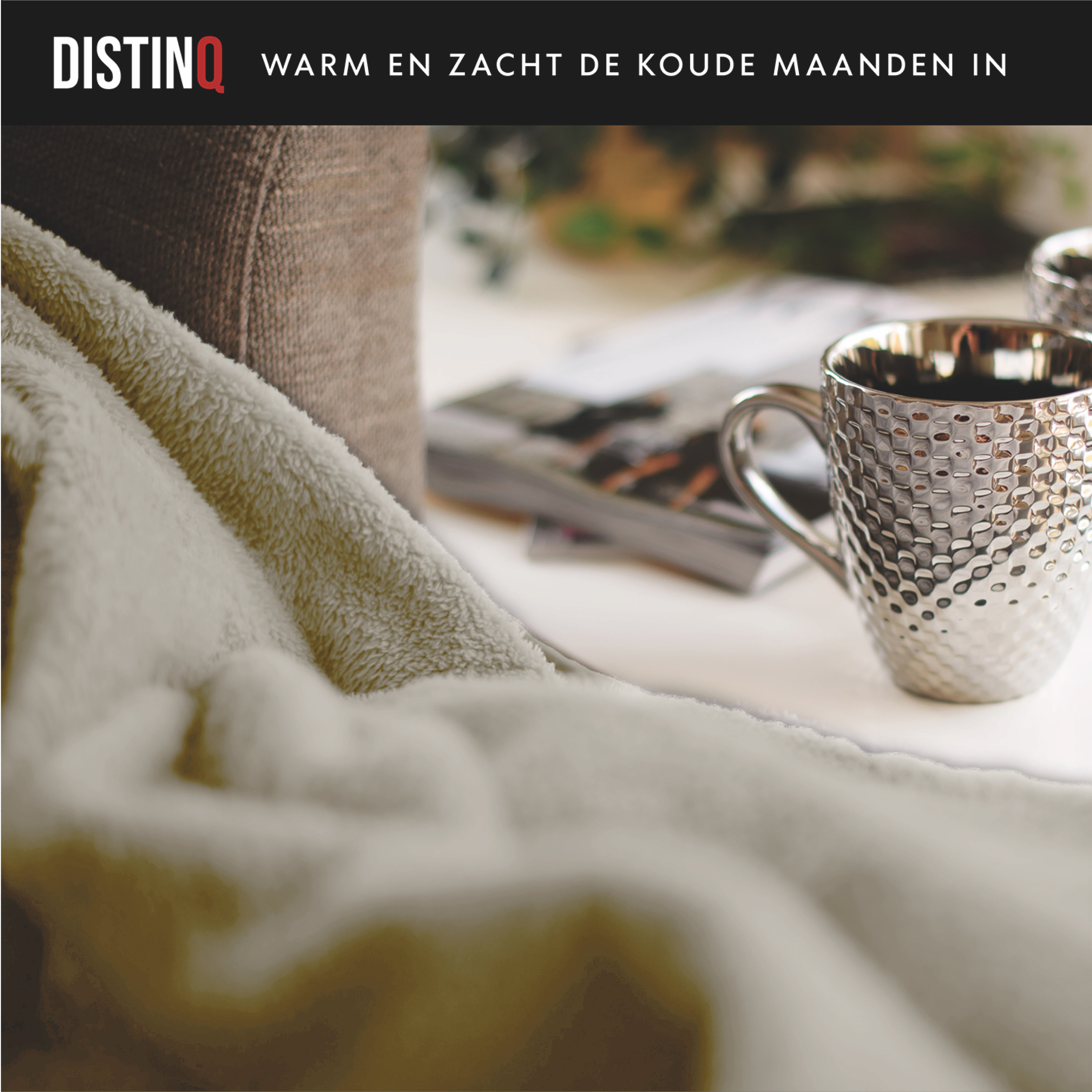 A mug, blanket, and magazine are on a table. The blanket is tan. The mug is silver.