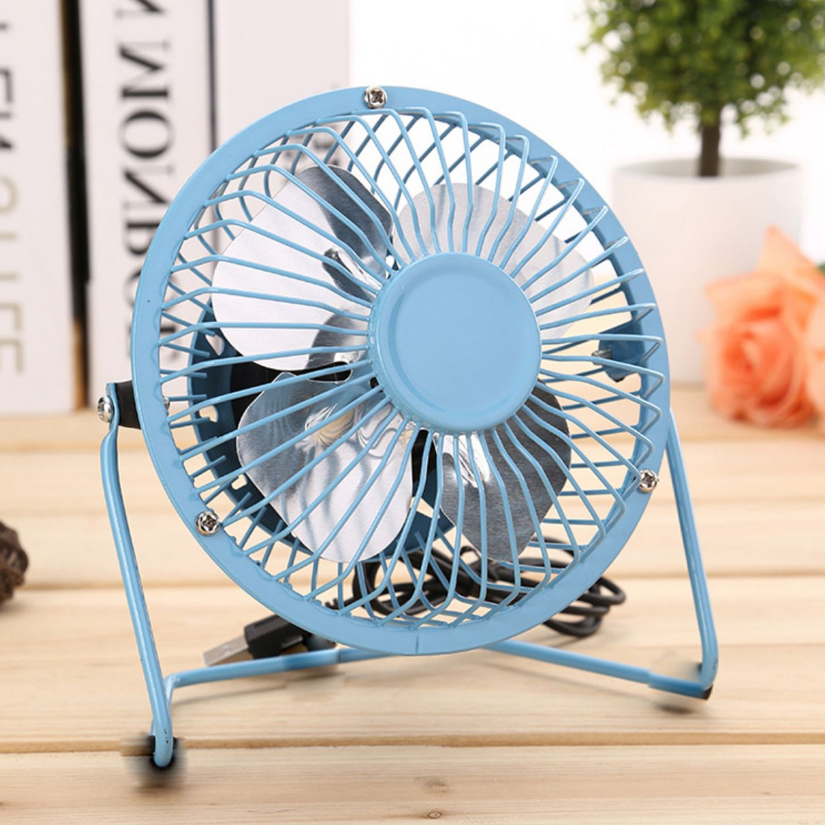 Blauer Mini-Ventilator mit Drahtkäfig. Auf einem Holztisch. Die Flügel sind blau.