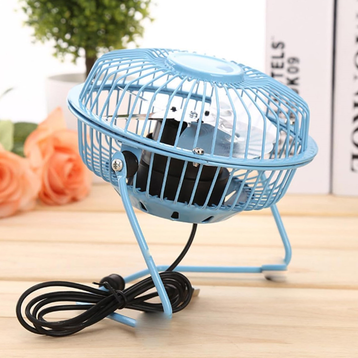 Blauer Schreibtischventilator auf Holzoberfläche. Der Ventilator hat einen blauen Käfig und ein schwarzes Netzkabel.