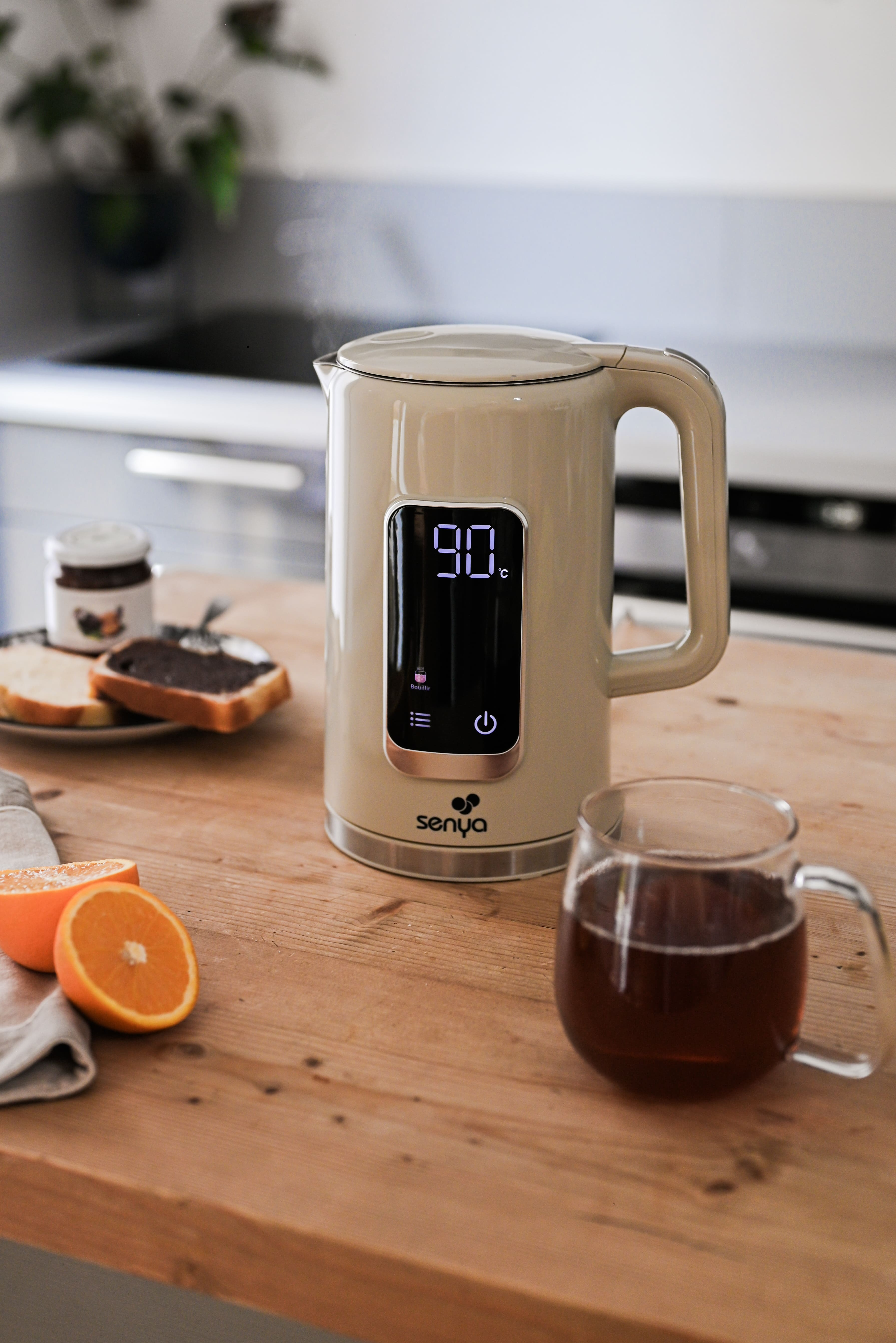 Bollitore elettrico beige con display digitale, su superficie in legno, con cibo.