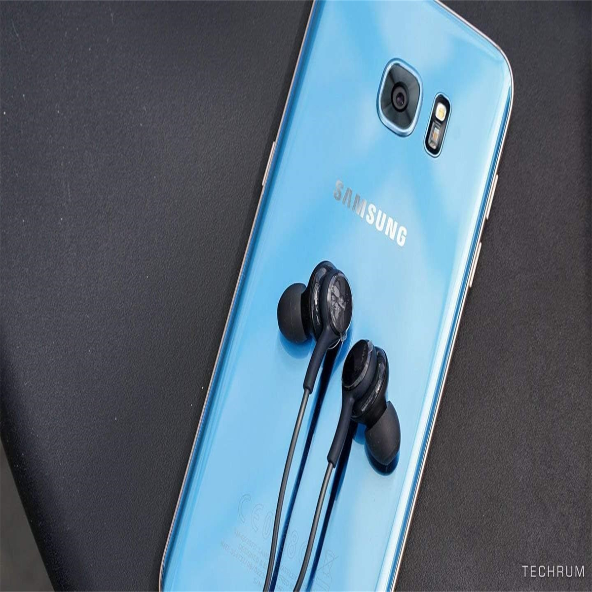 Ein blaues Samsung-Telefon mit schwarzen Kopfhörern auf dunkler Oberfläche.