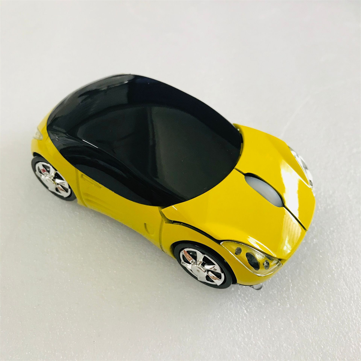 Gelbe, auto-förmige Computermaus mit schwarzem Oberteil und Chromrädern.