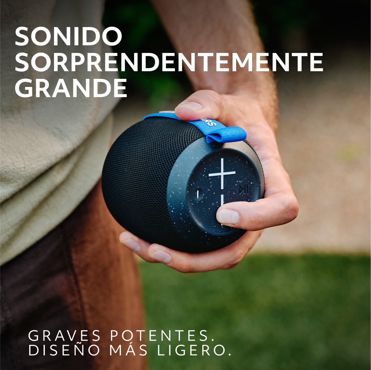 Czarny i niebieski głośnik trzymany przez dłoń, z tekstem na obrazie. Ciemne tło.