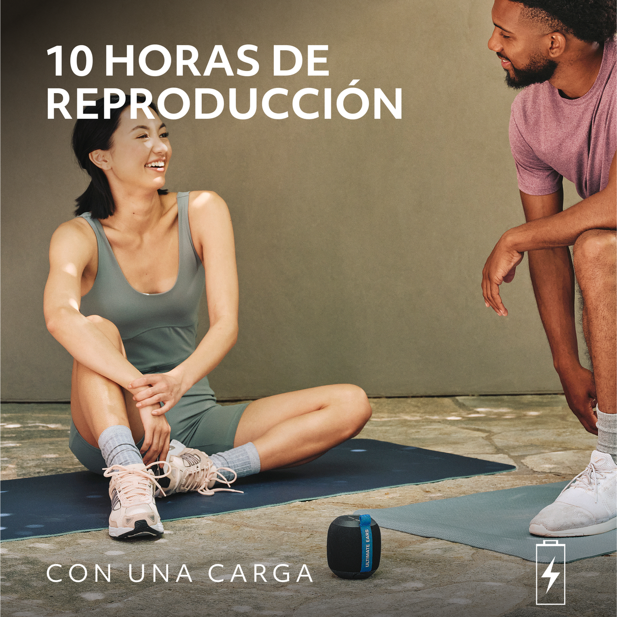 Dwie uśmiechnięte osoby. Głośnik i mały czarny głośnik leżą na macie.