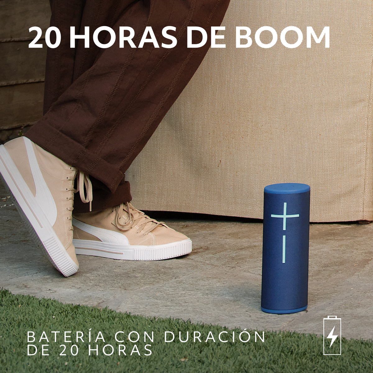 Un altoparlante blu vicino a una persona con pantaloni marroni e scarpe beige. Testo sull'altoparlante: '+' e '-'