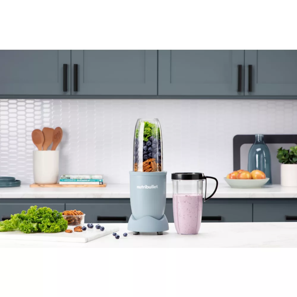 Un mixeur avec des ingrédients. Un verre avec un smoothie rose est à droite.