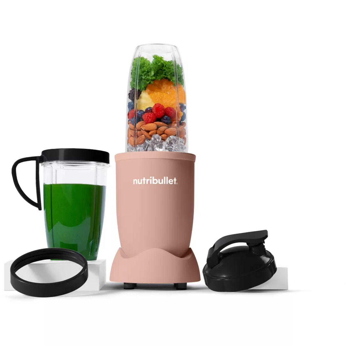 Blender Nutribullet ze składnikami: owoce, orzechy, lód. Zielony sok w filiżance obok.