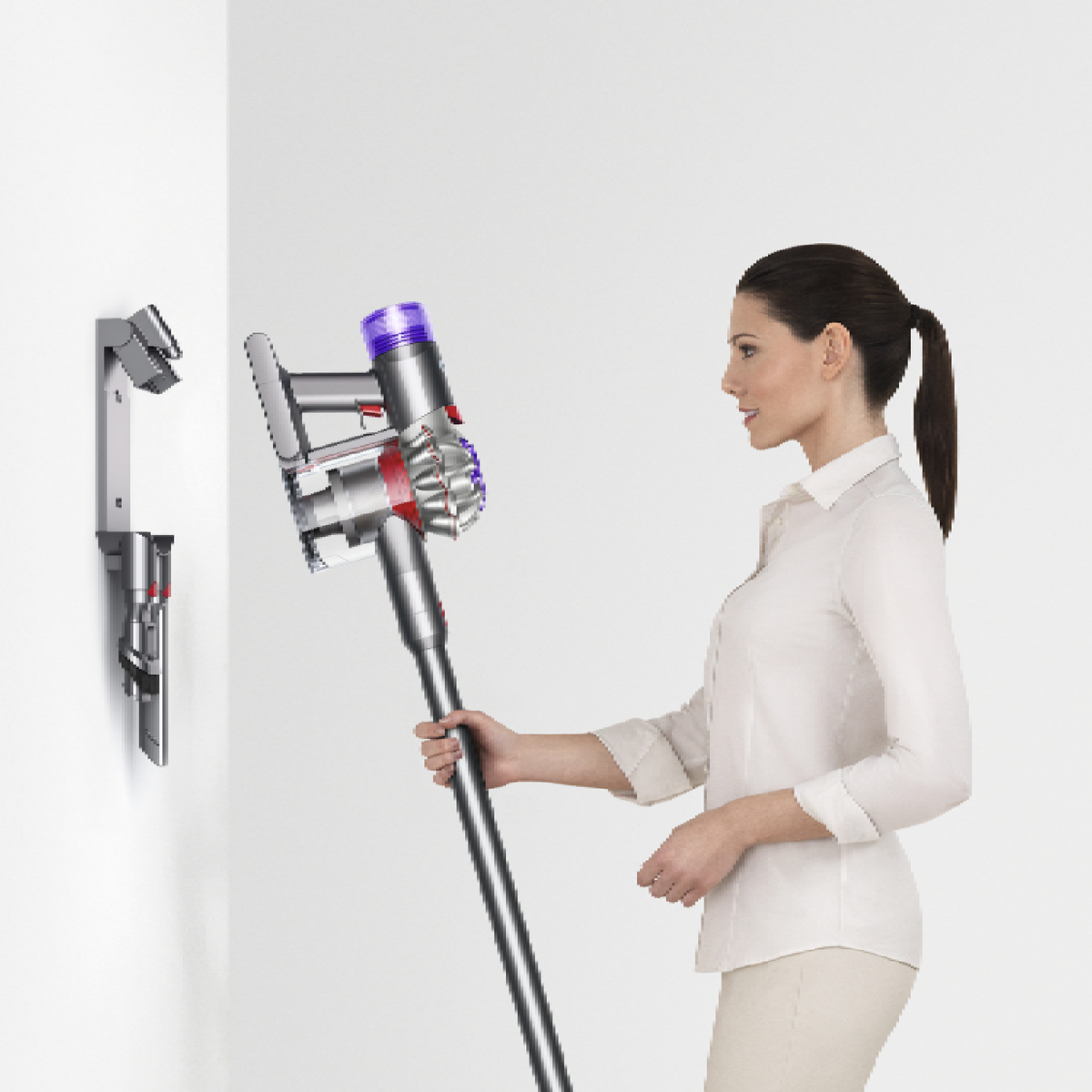 Kobieta trzyma odkurzacz, obok montowanej na ścianie stacji ładowania.