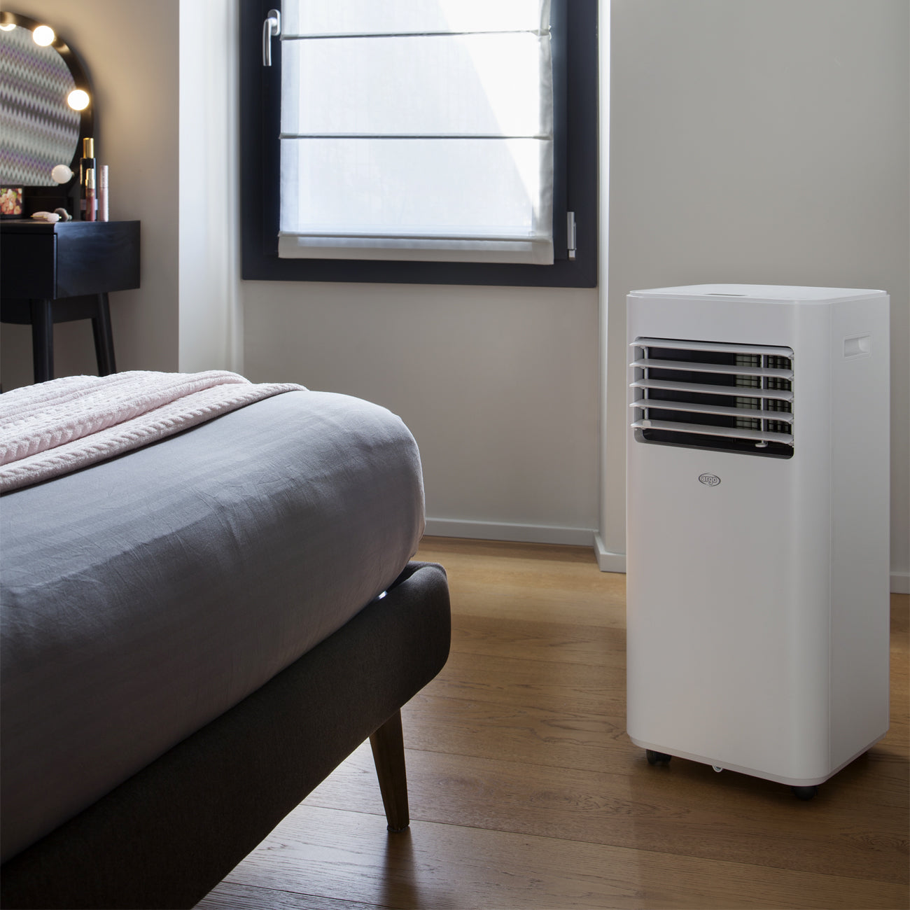 Un condizionatore portatile bianco in una stanza con un letto e una finestra.