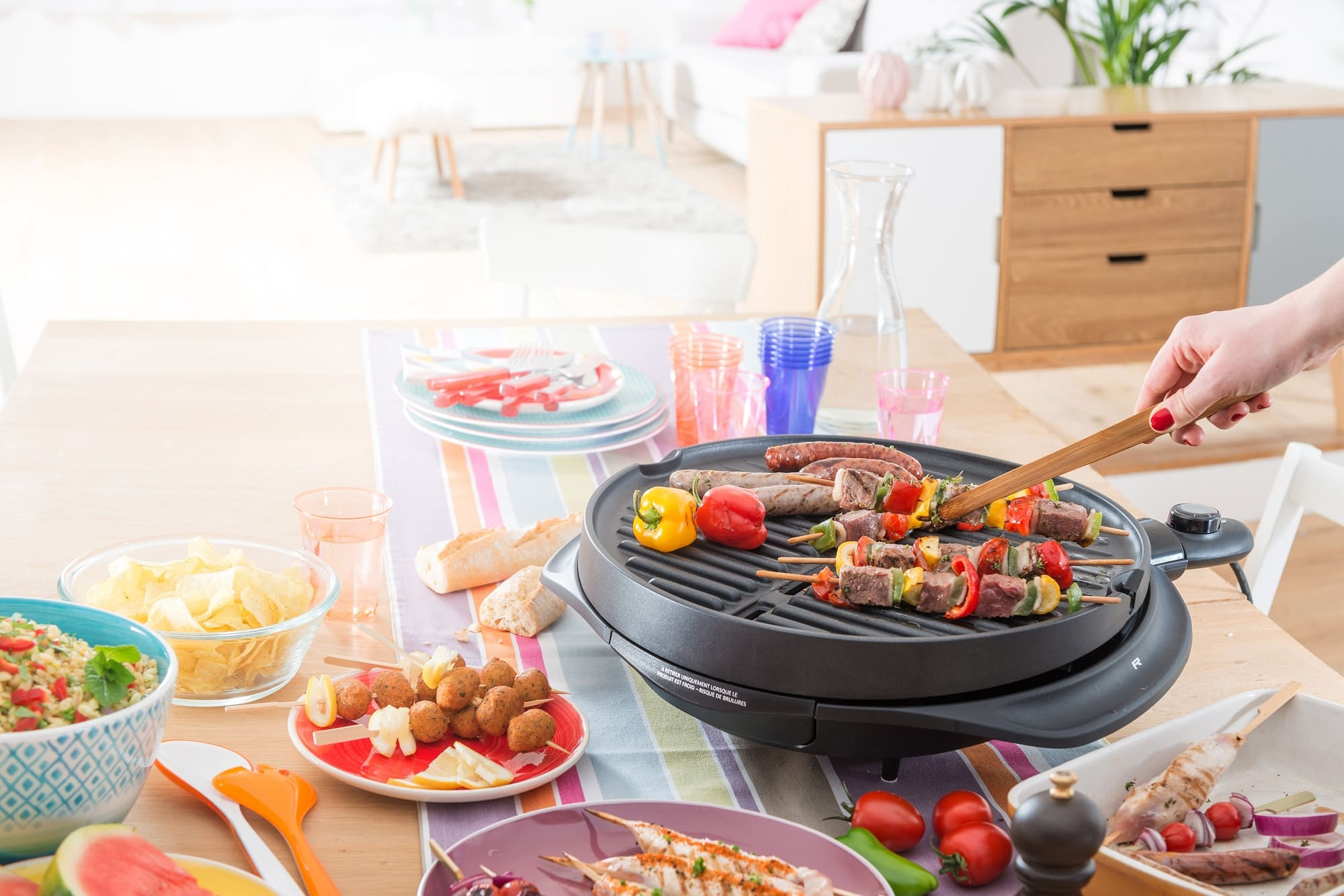 Eine Person grillt Spieße auf einem Elektrogrill, mit verschiedenen zubereiteten Speisen drumherum.