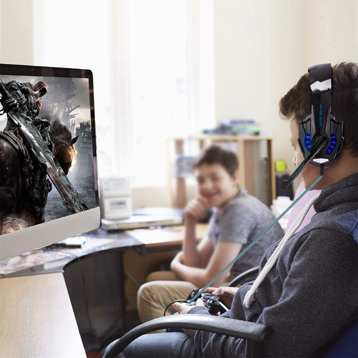 Eine Person mit Gaming-Headset spielt ein Spiel auf einem Monitor, mit einer anderen Person.