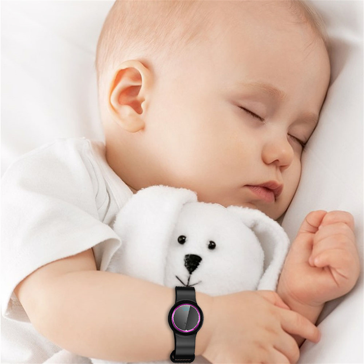 Baby schläft mit weißem Teddybär, trägt Smartwatch am Handgelenk.