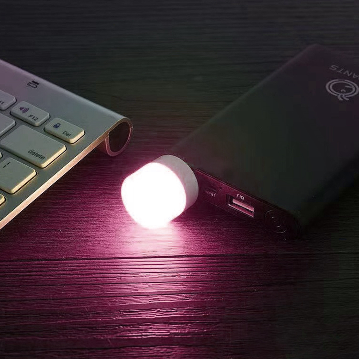 Eine weiße Tastatur und eine schwarze Powerbank mit einem kleinen, beleuchteten, zylindrischen Aufsatz auf Holzoberfläche.