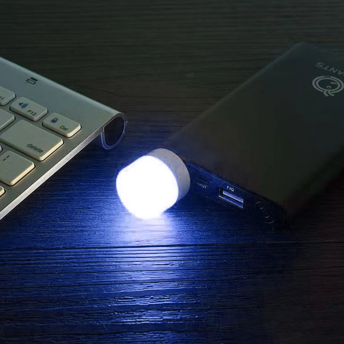 Eine Powerbank mit Taschenlampenfunktion. Links eine Tastatur. Die Szene ist auf einem Holztisch.