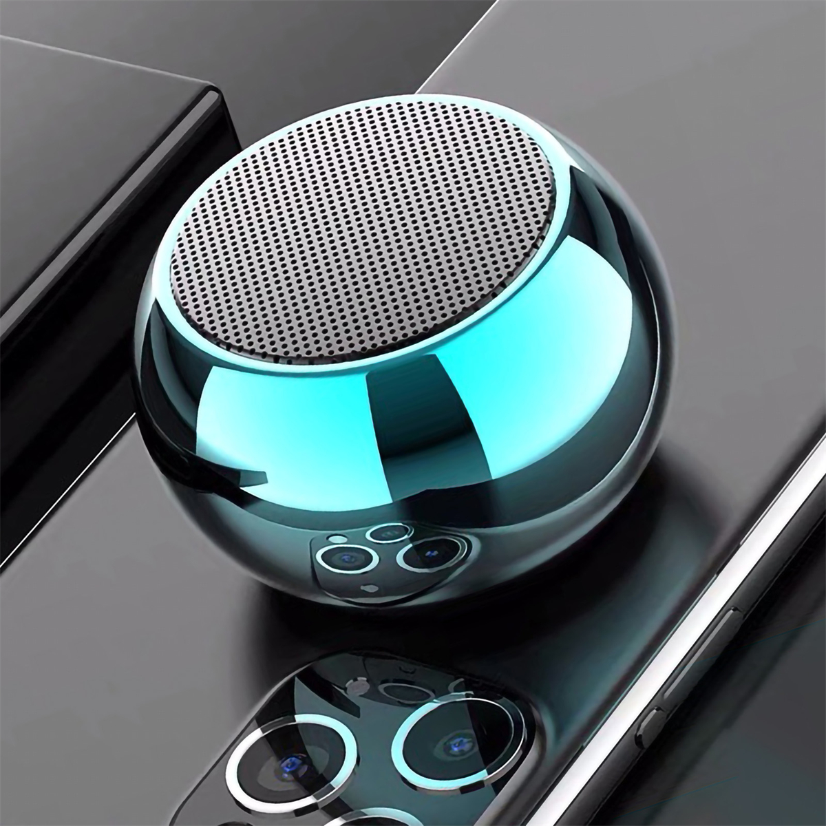 Silberner und blauer kugelförmiger Bluetooth-Lautsprecher auf schwarzer Oberfläche, der sich spiegelt.