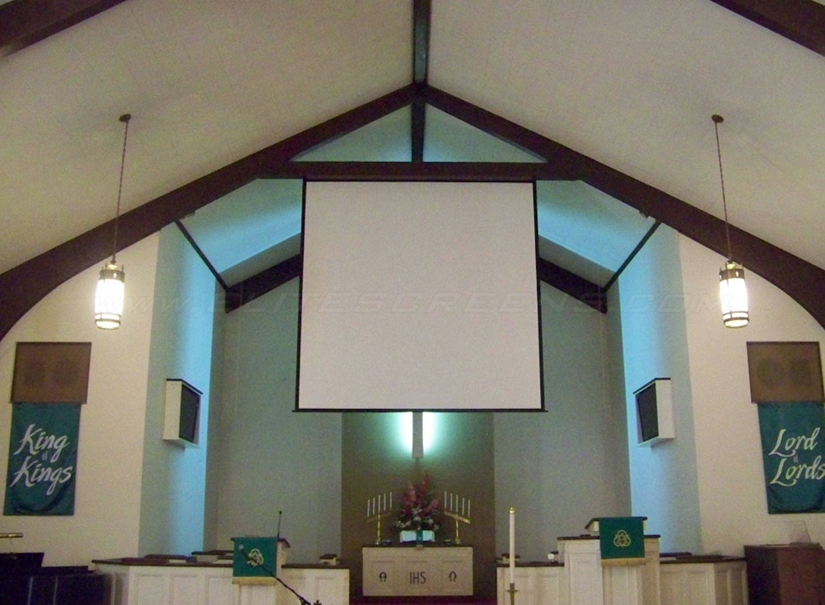 Kircheninnenraum mit weißer Leinwand, Bannern und Beleuchtung. Die Szene ist gut beleuchtet.