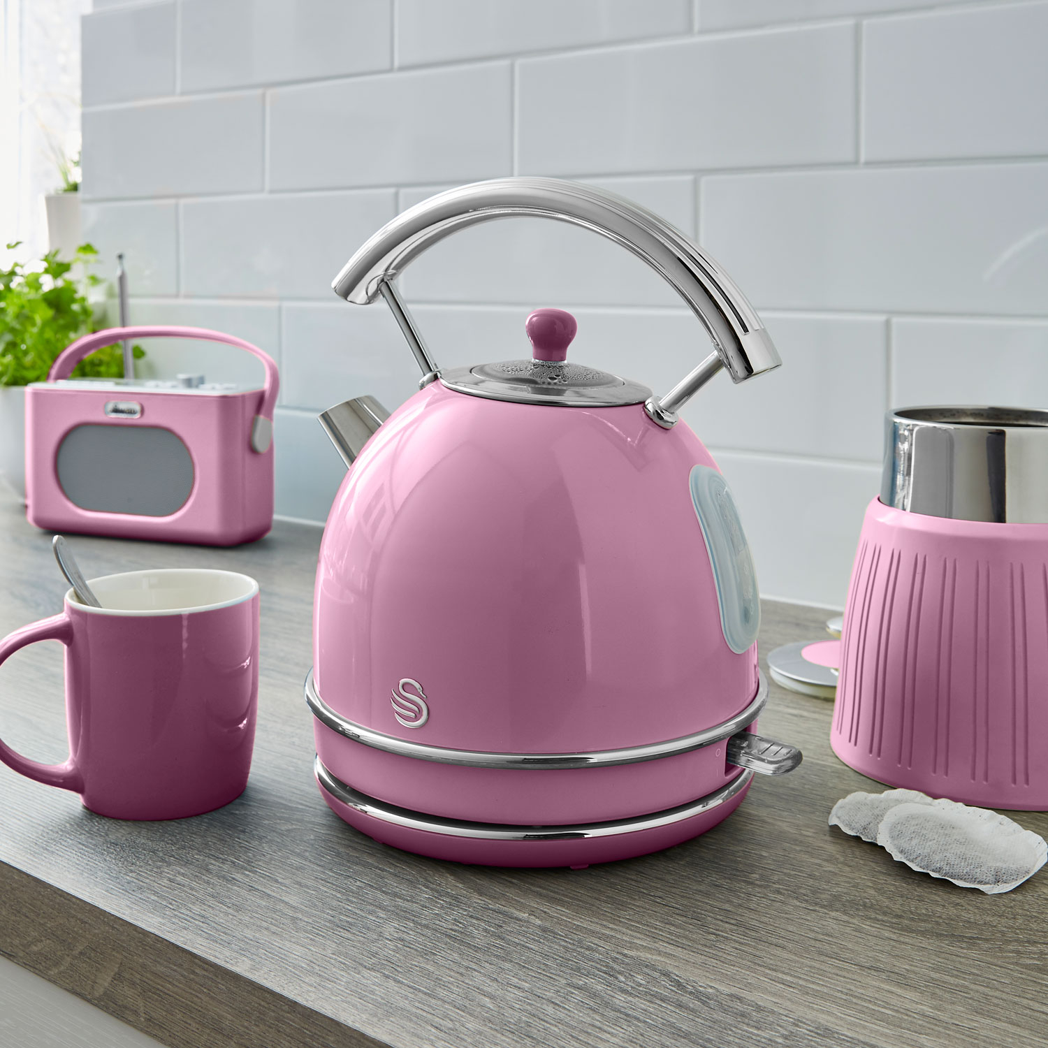 Hervidor, taza y radio rosas sobre superficie de madera. Bolsa de té cerca.