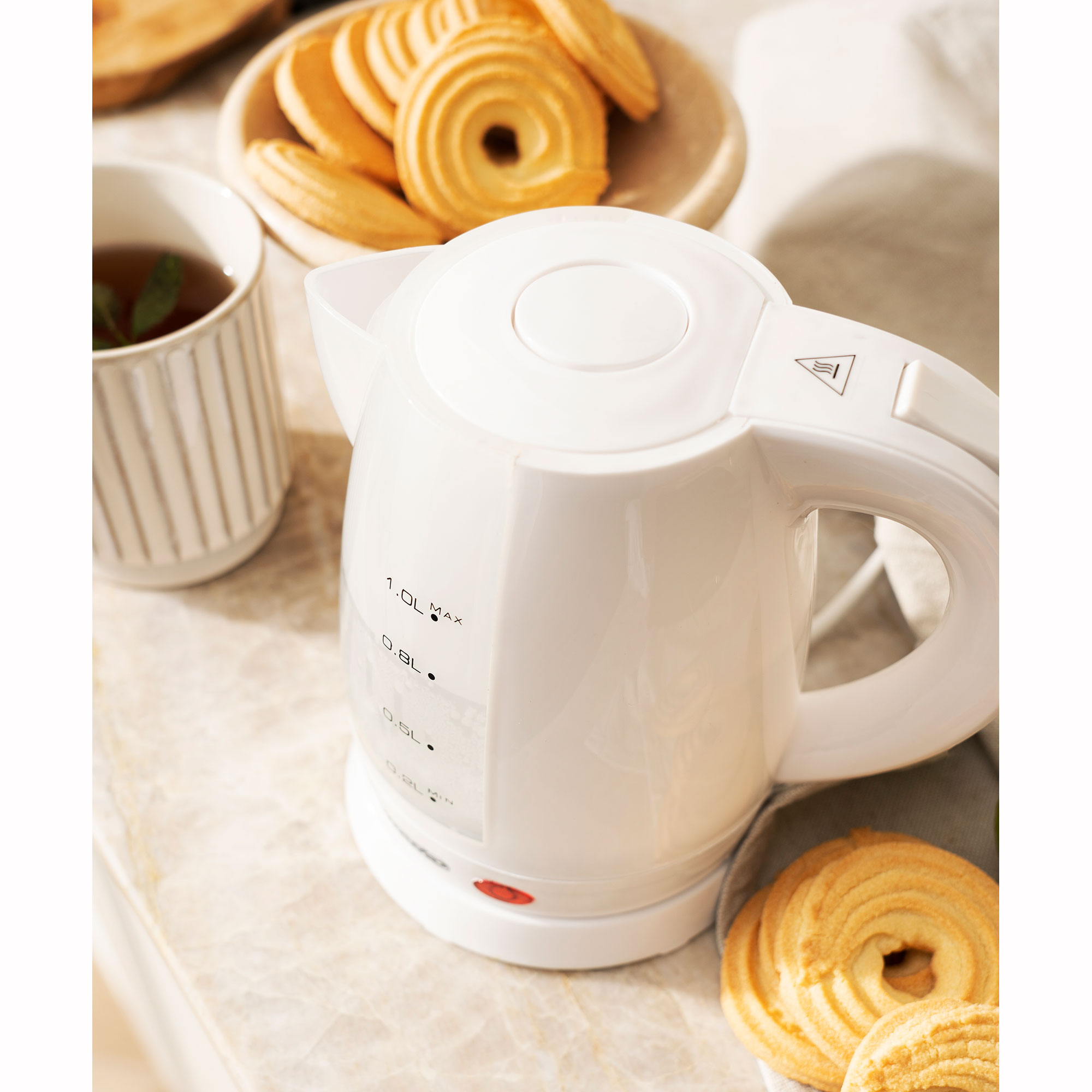 Hervidor blanco con marcas, cerca de galletas y una taza de té. Fondo blanco.