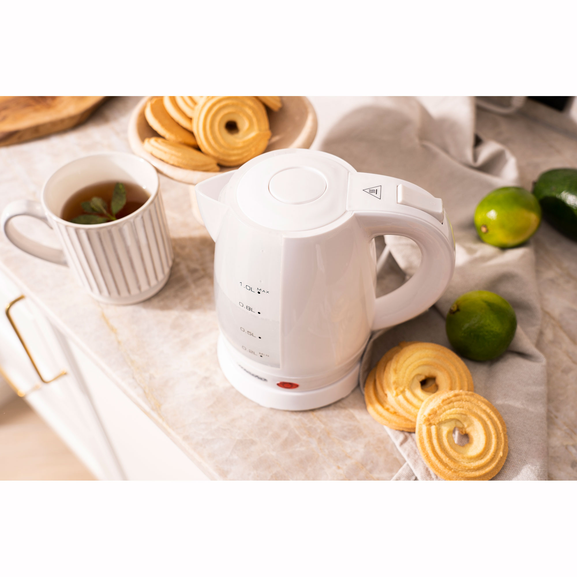 Hervidor eléctrico blanco con asa, rodeado de galletas, una taza de té y limas verdes.
