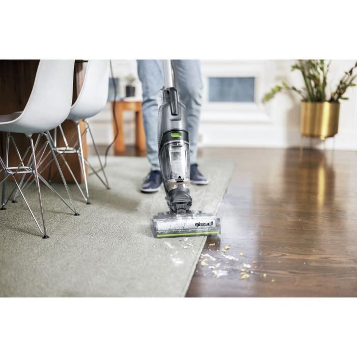 Une personne passe l'aspirateur sur un tapis avec un aspirateur. L'aspirateur est debout. Le sol est sale.