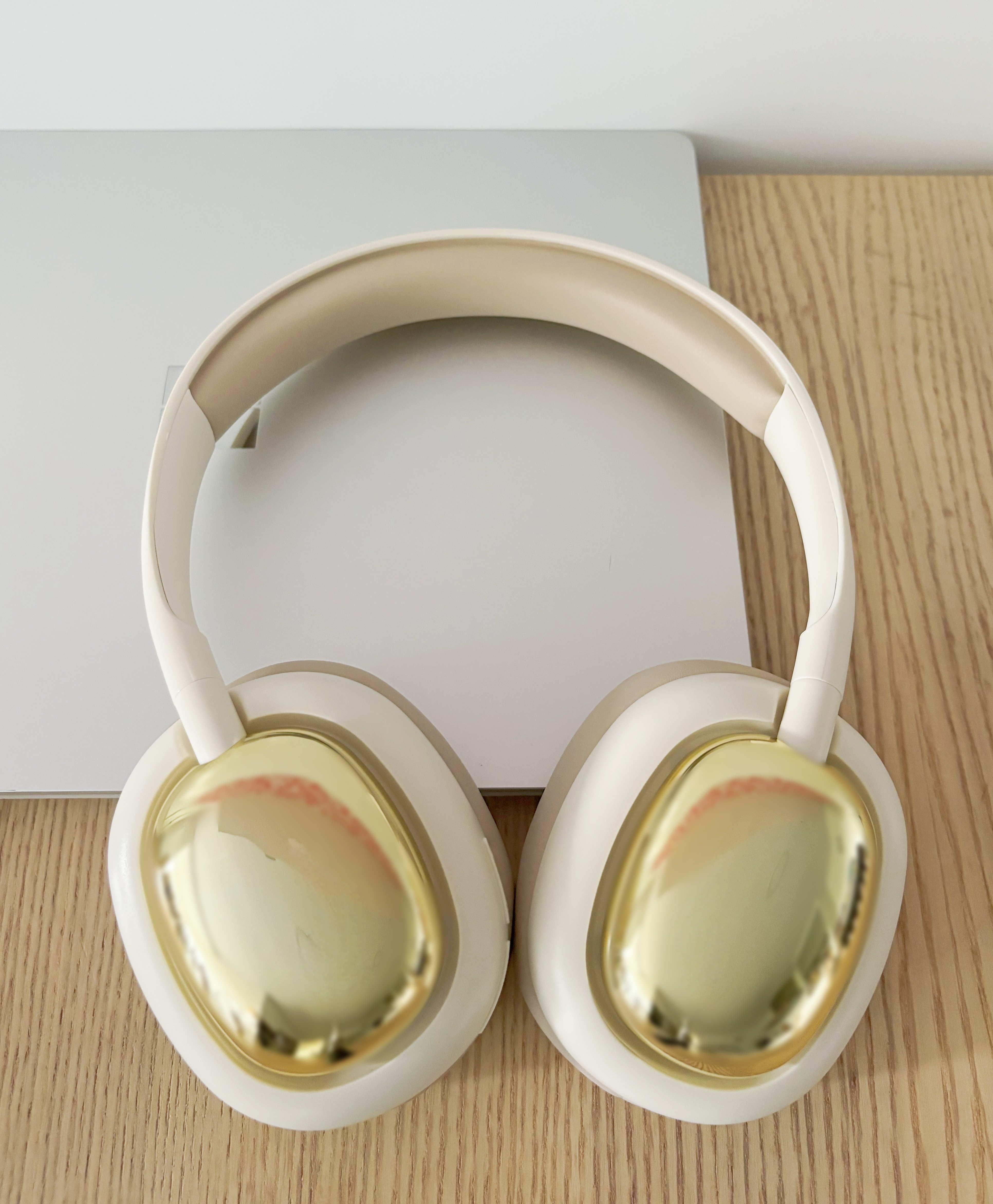 Auriculares beige y dorados sobre una mesa. Los auriculares están junto a un portátil plateado.